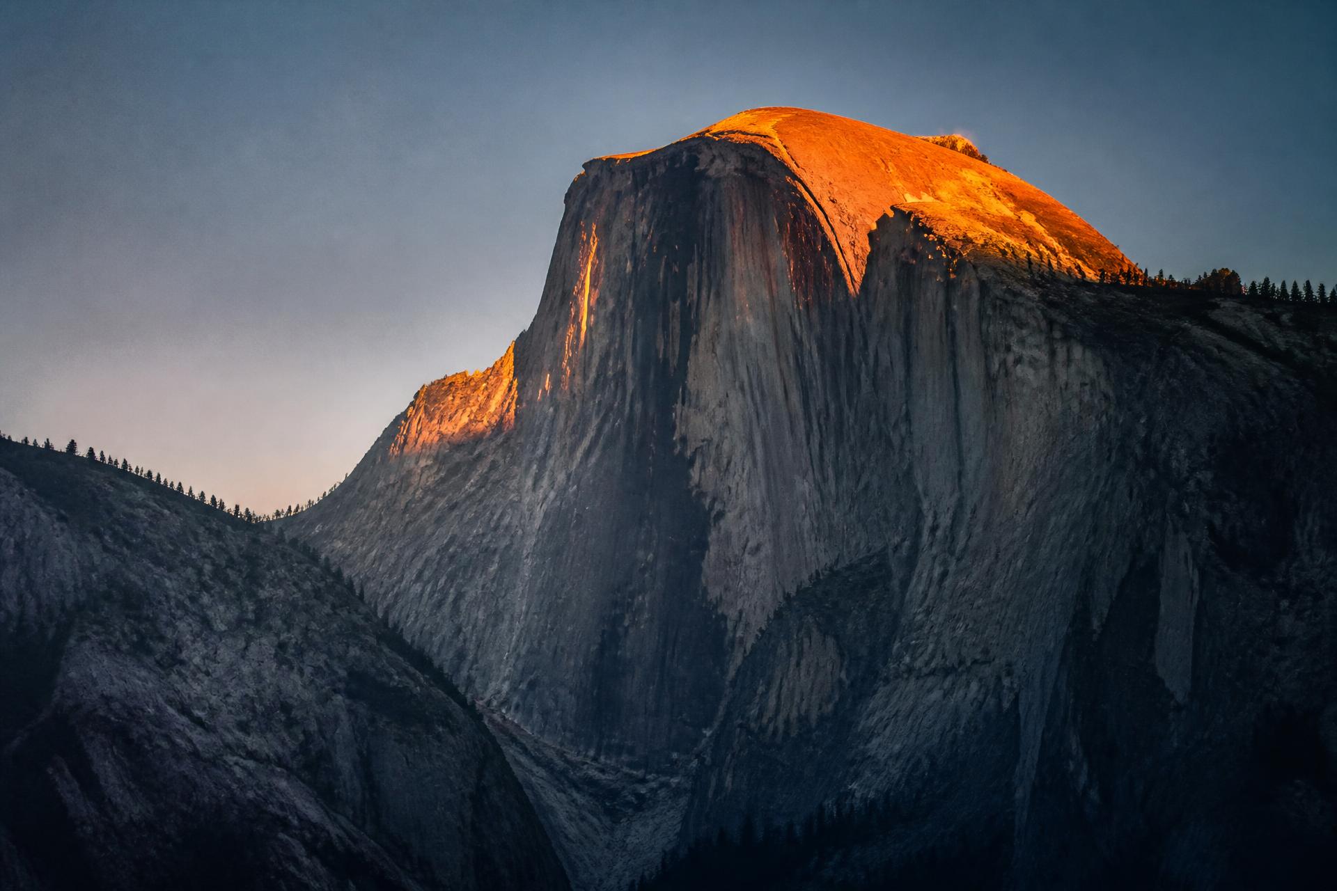 A granite big wall in Yosemite at first light, its summit lit by copper alpenglow